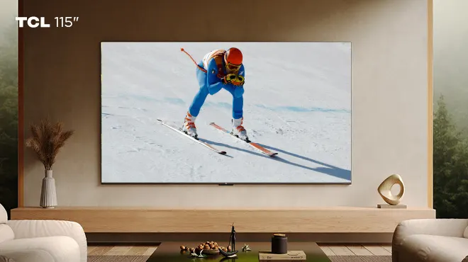 Grande schermo TV mostra giocatori di calcio che esultano su un campo verde. In primo piano un tavolino rotondo in legno.