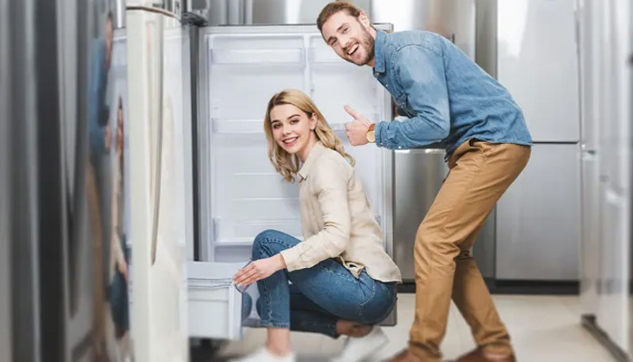 Uomo e donna sorridono guardando un frigorifero aperto in un negozio di elettrodomestici. L'uomo alza il pollice.