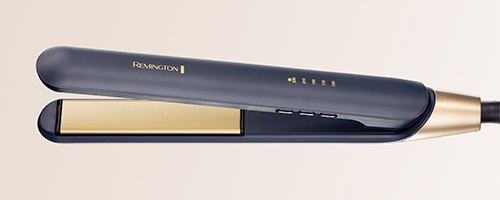 Piastra per capelli aperta, nera e oro, con marchio "Remington" visibile. Fondo crema.