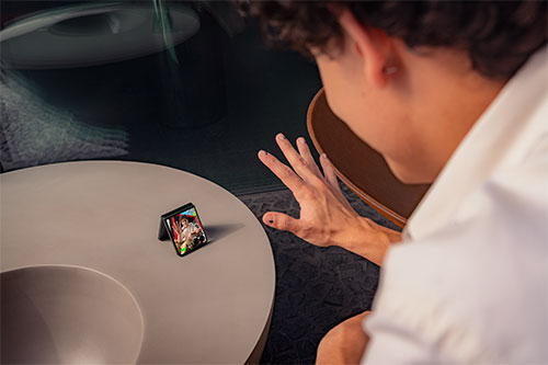 Un uomo guarda un telefono pieghevole aperto su un tavolo rotondo. La mano dell'uomo è sollevata verso il telefono.