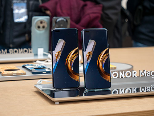 Due smartphone con schermi blu e dettagli dorati su supporti riflettenti, con accessori e scritte "HONOR Mag" visibili.
