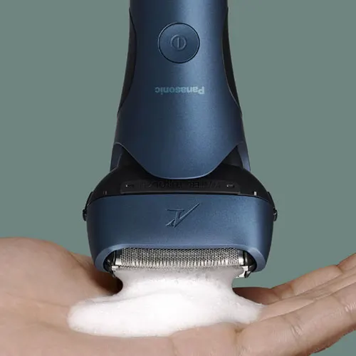 Rasoio blu su una mano con schiuma bianca. Sfondo grigio.