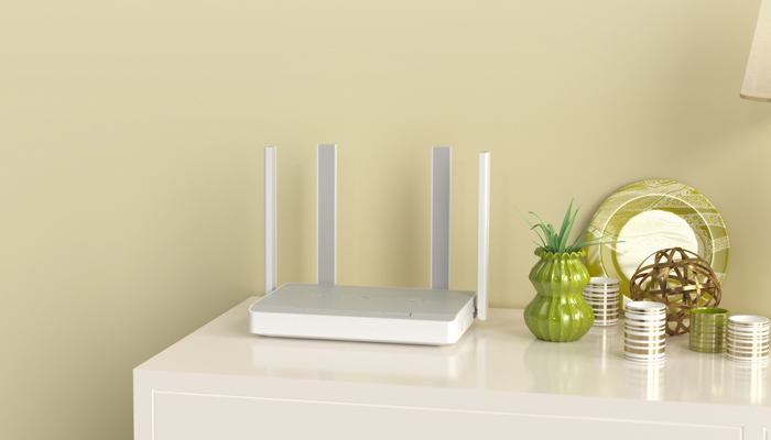 Un router bianco con quattro antenne è su un tavolo bianco. Accanto, un vaso verde, un piatto decorativo e piccoli oggetti dorati.