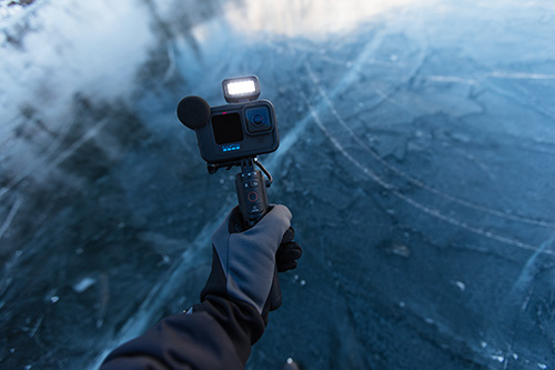 Una mano guantata tiene una action camera su ghiaccio blu screziato. La luce � accesa sulla fotocamera.