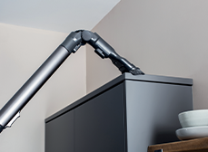 Aspirapolvere grigio pulisce la parte superiore di un mobile scuro in una stanza con pareti chiare. Piatti bianchi sullo sfondo.