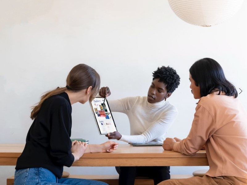 Tre persone siedono a un tavolo di legno e guardano un tablet. Una persona indica lo schermo del tablet.