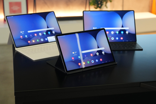 Tre tablet su un tavolo nero. Gli schermi mostrano un'interfaccia utente blu con icone colorate. Sullo sfondo, oggetti sfocati.