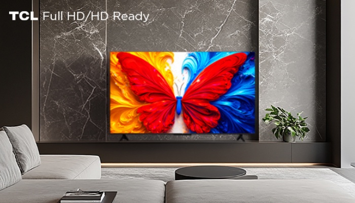 Un televisore TCL Full HD/HD Ready posizionato su un mobile nero specchiato davanti a una parete in marmo scuro. Sullo schermo è visualizzata una farfalla colorata con ali rosse, gialle e blu.