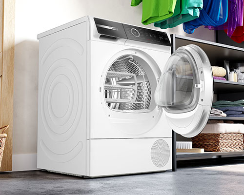 Asciugatrice bianca con obl� aperto, cesto metallico visibile. Scaffale grigio con cesti e vestiti sullo sfondo.