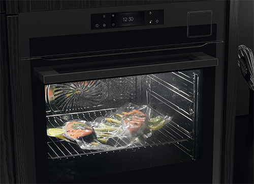 Forno nero con cibo confezionato su una griglia. Una ventola è visibile sul retro. Un timer digitale si trova in alto.