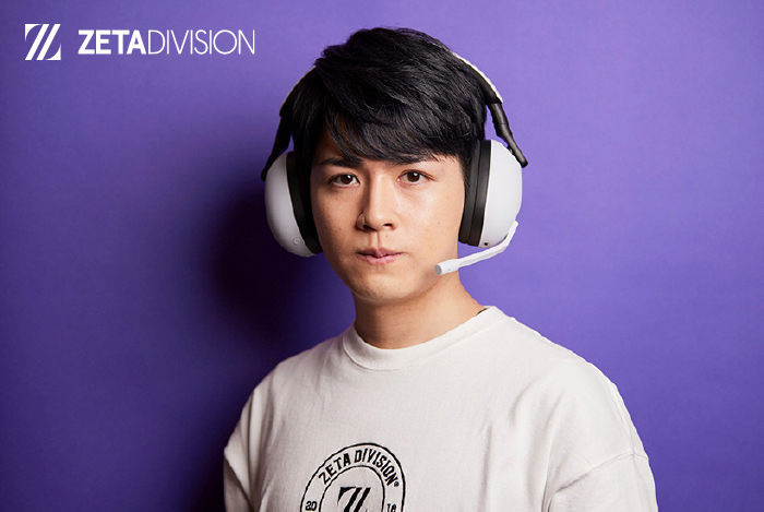 Uomo con cuffie bianche e microfono, indossa una maglietta bianca con logo su sfondo viola.