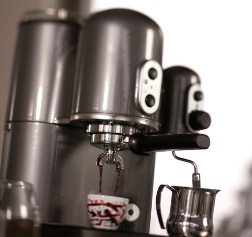 Macchina da caff� in metallo con tazza decorata e brocca in metallo, su sfondo chiaro.