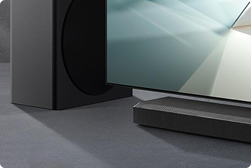 Primo piano di un televisore con soundbar nera e subwoofer su una superficie grigia.