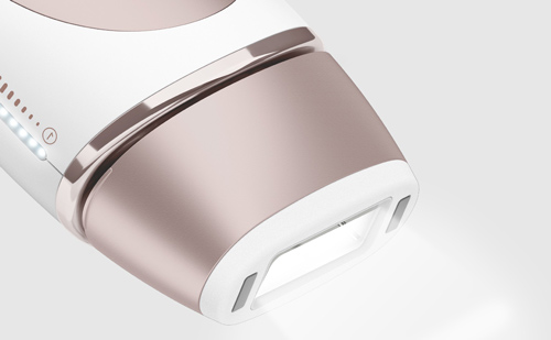 Dispositivo bianco e rosa per la depilazione a luce pulsata su sfondo grigio chiaro, con luce intensa che emana dal sensore.