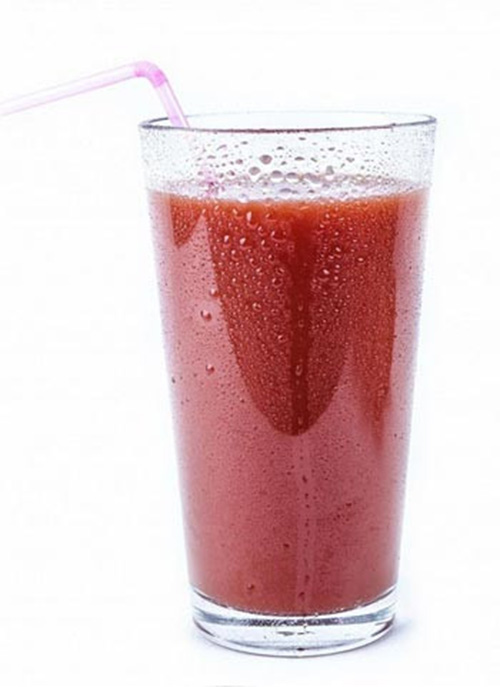 Su sfondo bianco, un bicchiere trasparente riempito con un liquido rosso e una cannuccia rosa.