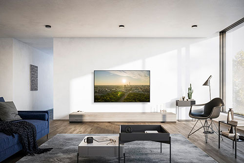 Soggiorno con divano blu, tavolino, tappeto grigio e TV che mostra un paesaggio. Sedia nera e finestra sulla destra.