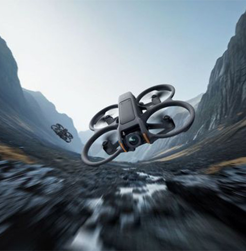 Un drone nero con eliche in volo tra montagne grigie. Un altro drone pi� piccolo � visibile in lontananza.