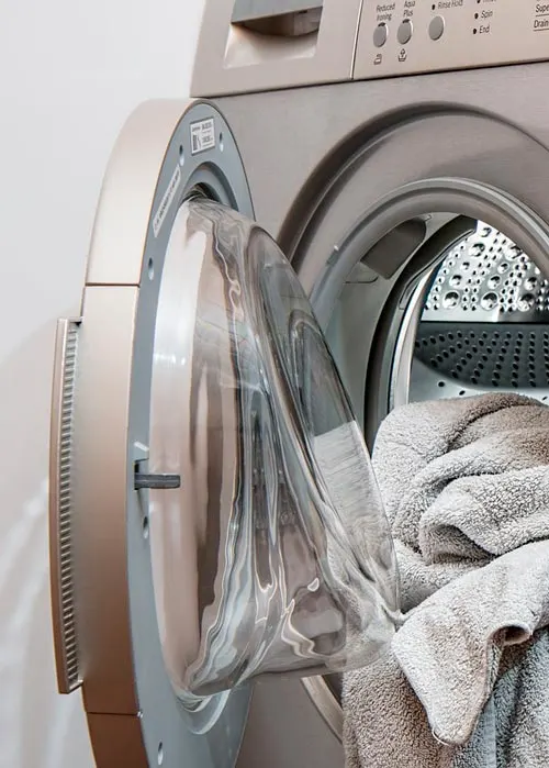 Lavatrice aperta con asciugamani grigi all'interno. Lo sportello � trasparente e mostra il cestello metallico.