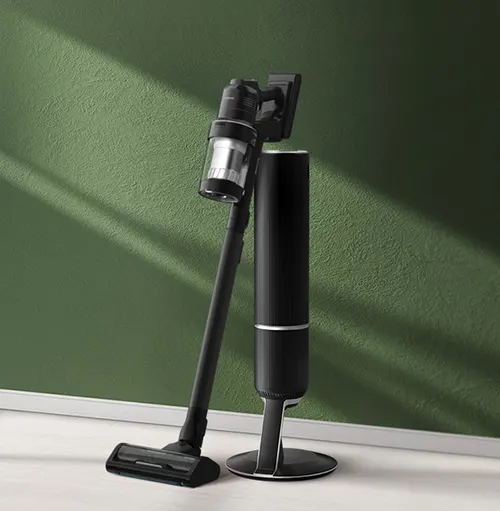 Aspirapolvere nero accanto a supporto verticale, su pavimento chiaro, contro muro verde.