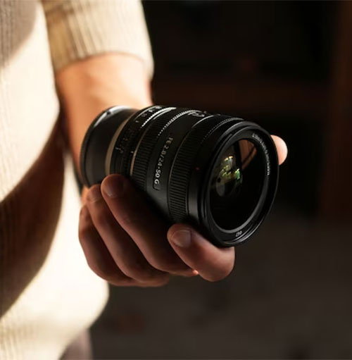 Mano che tiene un obiettivo nero. L'obiettivo ha anelli multipli. Sfondo scuro.