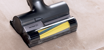 Primo piano di una spazzola di aspirapolvere nera e gialla su una superficie marrone chiaro.