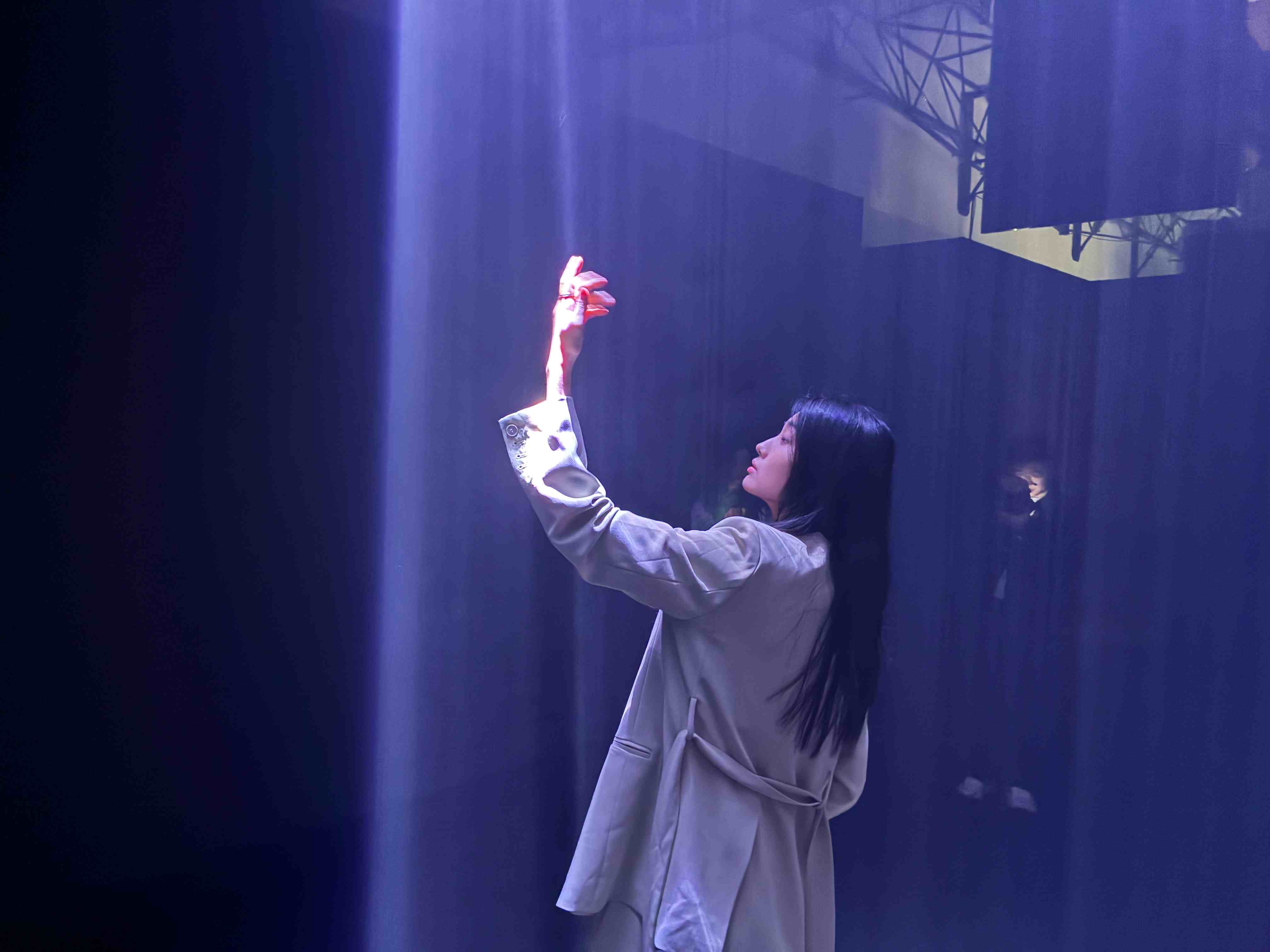 Una donna con una giacca chiara alza una mano verso un raggio di luce blu in uno spazio buio.