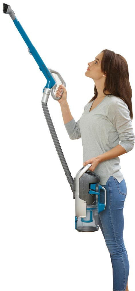 Donna in jeans azzurri usa aspirapolvere verticale blu per pulire in alto.