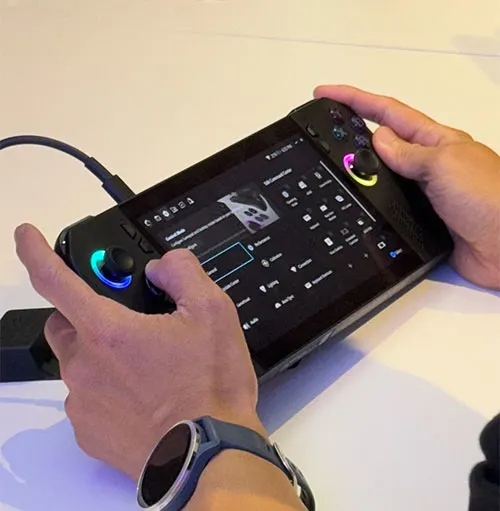 Mani tengono una console da gioco nera con schermo acceso. Un cavo � collegato a sinistra. Un orologio � al polso.