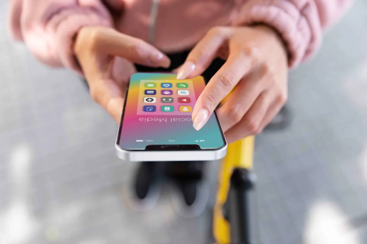 Dettaglio di mani che usano un telefono con icone colorate su uno sfondo sfumato. Parte di un oggetto giallo visibile sullo sfondo.