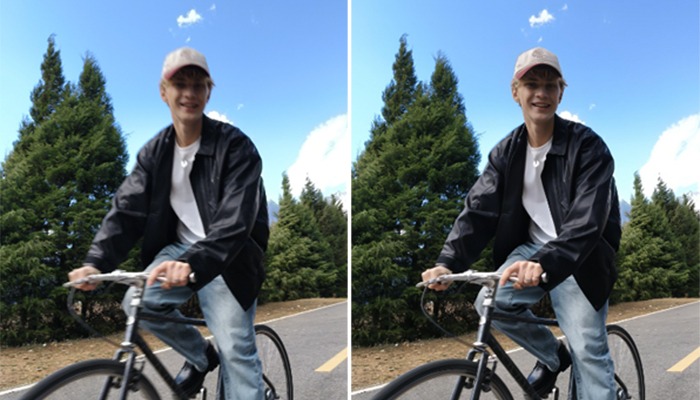 Un uomo in bici su strada asfaltata, indossa giacca nera, jeans e cappello. Alberi sullo sfondo e cielo azzurro.