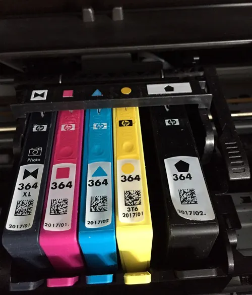 Cinque cartucce per stampante HP colorate: nero, magenta, ciano e giallo con etichette "364" e codici QR.