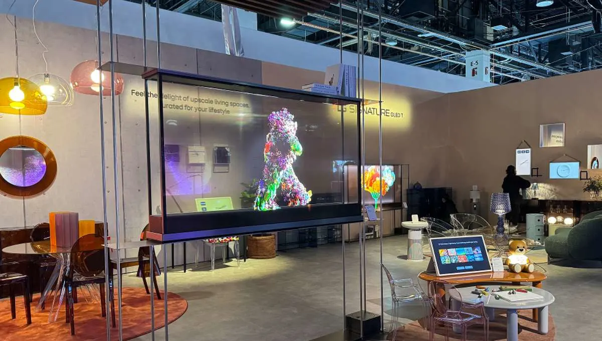 Interno di uno stand espositivo con tavoli, sedie, lampade e schermi trasparenti che mostrano immagini colorate.