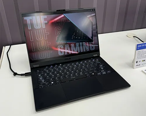 Un computer portatile nero aperto mostra la scritta "TUF GAMING" sullo schermo su un tavolo bianco.