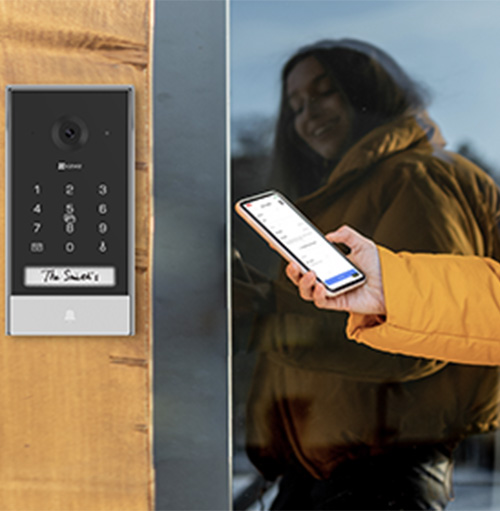 Donna con giacca marrone che tiene un telefono vicino a una tastiera numerica montata su una porta di legno.