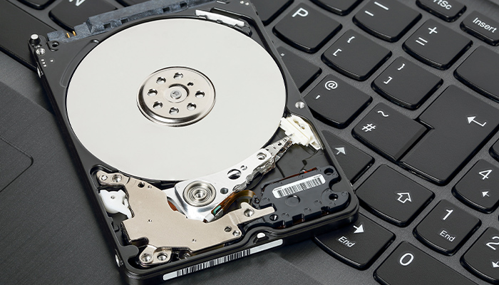 Disco rigido aperto su una tastiera nera. Il disco è argento e nero, rivelando componenti interni.
