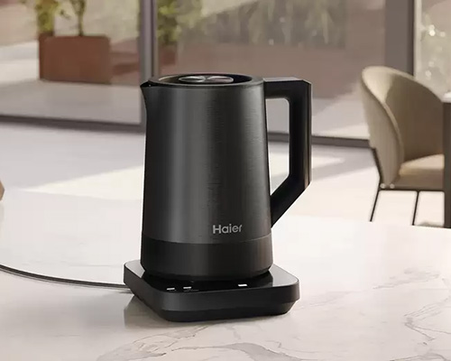Bollitore nero 'Haier' su base nera su un ripiano. Una sedia e una finestra sono sullo sfondo.