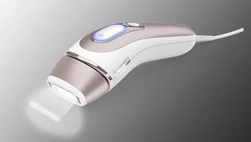 Dispositivo di depilazione bianco e grigio con cavo, emette luce da un'apertura frontale su sfondo sfumato grigio.