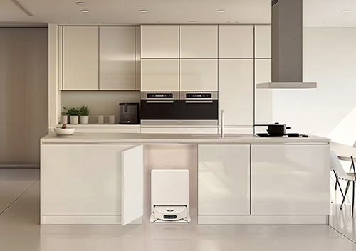 Cucina moderna con mobili bianchi, forno nero e cappa grigia. Robot aspirapolvere sotto il bancone.