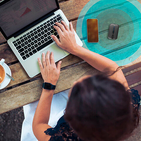 Donna che usa un laptop su un tavolo di legno con telefono, mouse e tazza.