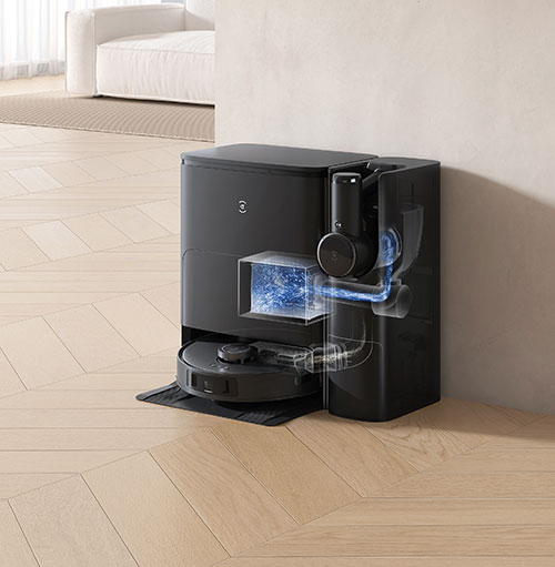 Aspirapolvere robot nero con stazione di ricarica su pavimento in legno chiaro. Divano bianco sullo sfondo.