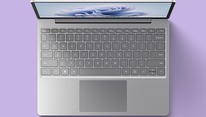 Vista dall'alto di un laptop aperto su sfondo viola. Si vedono lo schermo, la tastiera grigia e il trackpad.