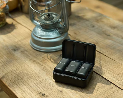 Su un tavolo di legno sono presenti una lanterna ad olio e una scatola nera aperta con tre microfoni Sony.