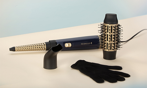 Ferro arricciacapelli blu con accessori, tra cui spazzola rotonda, ugello concentratore e guanto nero su sfondo chiaro.