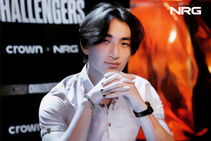 Un uomo in camicia bianca, con le mani giunte, posa davanti a uno sfondo nero e arancione con loghi bianchi.