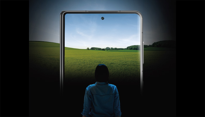 Una persona guarda un telefono che mostra un prato verde e un cielo azzurro, su uno sfondo scuro.