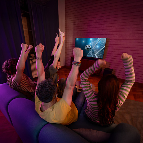 Due donne in interni con pareti rosse con scritta "GO LET'S GO". Una donna indica verso l'alto, l'altra indossa una giacca marrone.