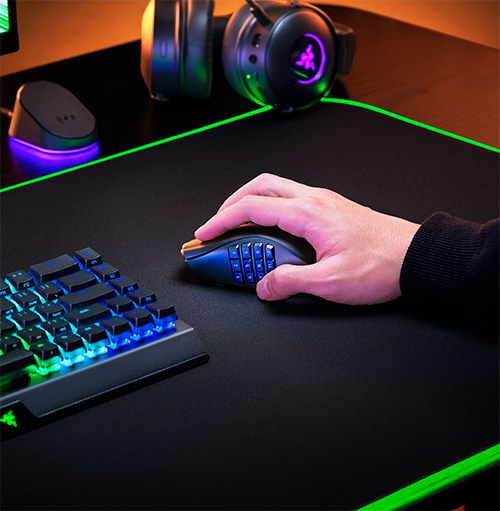 Su una scrivania nera con bordi verdi, una mano usa un mouse da gioco. Cuffie e tastiera sono visibili.