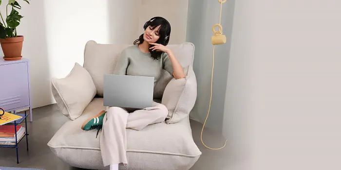 donna seduta su una poltrona, ha il portatile in mano e delle cuffie in testa.