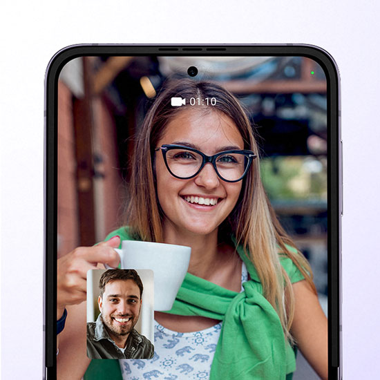 Schermo di smartphone: donna sorridente con occhiali tiene una tazza bianca durante una videochiamata con un uomo.