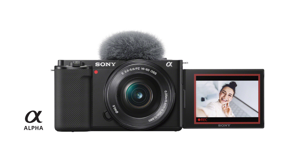 Fotocamera nera Sony Alpha con microfono e schermo LCD che mostra una persona sorridente. Logo Alpha in basso a sinistra.